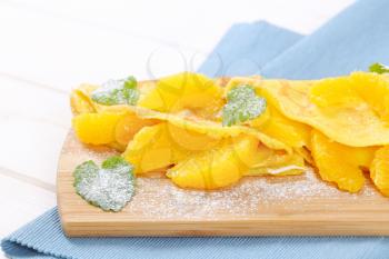 thin pancakes (crepes) with fresh orange slices on wooden cutting board - close up