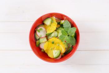 bowl of radish and cucumber salad with slices of orange