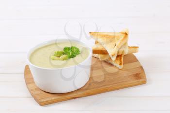 bowl of Brussels sprouts soup with toast on wooden cutting board
