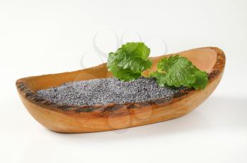black poppy seeds in boat-shaped wooden bowl on white background
