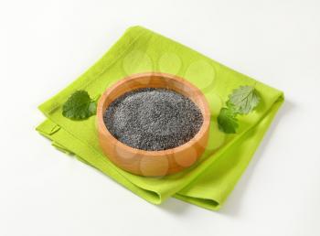 black poppy seeds in wooden bowl on green placemat