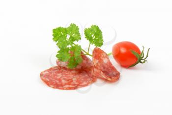 thin slices of salami with parsley and cherry tomato on white background