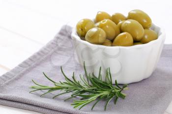 bowl of green olives with fresh rosemary on grey place mat - close up