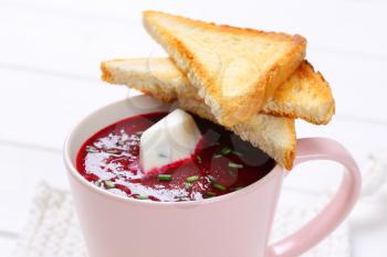 cup of beetroot cream soup with toast on white table mat - close up