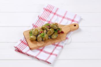 pile of marinated green olives on wooden cutting board