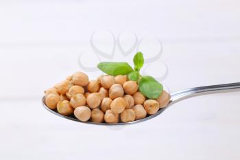 spoon of raw chickpeas on white wooden background
