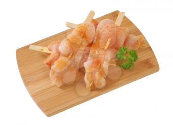 raw chicken skewers on wooden cutting board