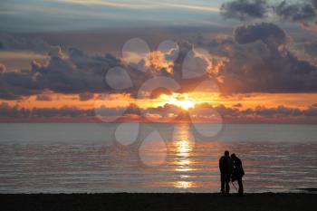 Silhouettes of two unidentifiable people on the beach taking photos of sunset over the sea