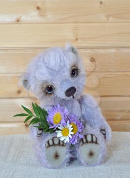 Handmade, the sewed toy: teddy-bear Chupa with a bouquet before a wooden wall