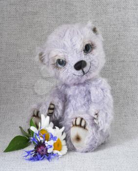 Handmade, the sewed toy: lilac teddy-bear with a bunch of flowers at feet