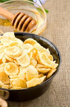 bowl of corn flakes and honey on wooden background