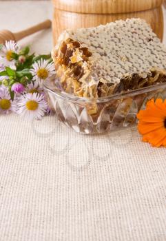 honey, honeycomb in pot, stick and flowers on sacking