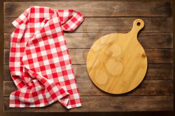 pizza cutting board and kitchen napkin cloth at rustic wooden plank board background, top view