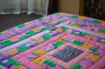 Blanket on a bed from bright pieces of a fabric.