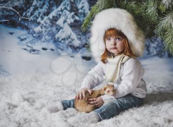 The child is sitting in the snow under the tree.