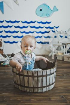 Little one-year-old child is seated in a wooden basin.