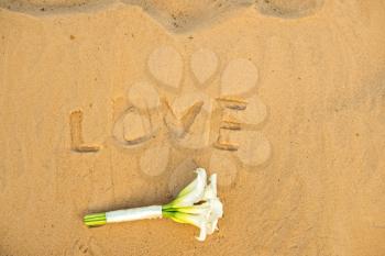 Word love on sand and a bouquet lying nearby.