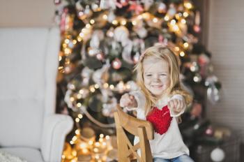 A little girl with a red heart on the clothes sitting in front of the tree.