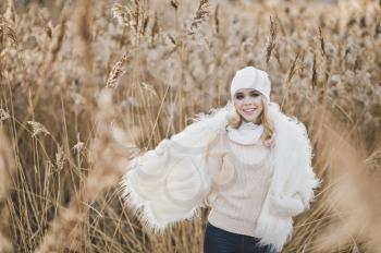 Close-up portrait of girl in white furry jacket and hat in the winter among the reeds.