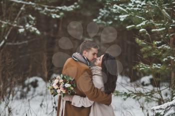 The couple gently kiss each other on the background of snow-covered forest.