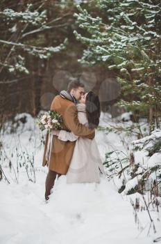 The couple gently kiss each other on the background of snow-covered forest.