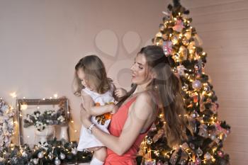 The girl turns the baby around the glittering Christmas tree.