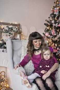 The daughter and mother sitting in a chair near the Christmas tree.