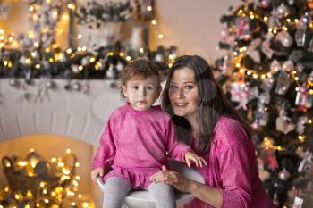 Portrait of mother with daughter on the Christmas tree in sparkling lights.