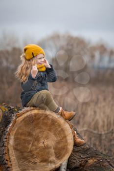 The child is sitting on the felled trunk of a large tree.