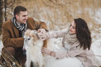 A guy and a girl petting a dog in the winter red grass.
