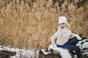 Portrait of a girl sitting in the winter on a fallen tree in the reeds by the lake.