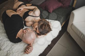 Husband and wife look each other in eyes lying down on bed.