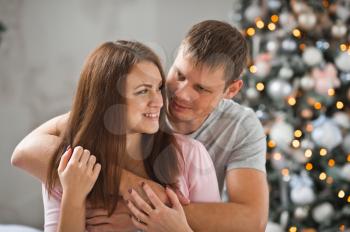 Newlyweds gently hugging on the background of the Christmas tree.