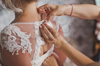 Mothers hands fasten wedding dress on her daughter.