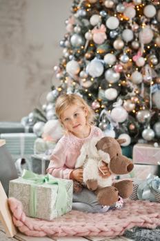 Happy child hugging a toy sitting around the Christmas tree.