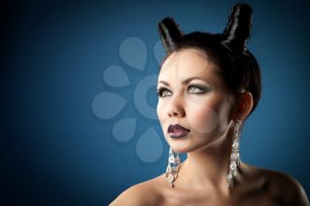 The girl in the image of the demon-tempter and hair in the form of horns. Photo taken in the studio on a background.