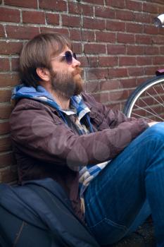 man traveler with a backpack and a bicycle sitting near the brick wall