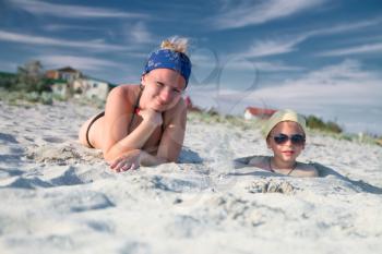 mother lies on the beach next to the child buried in the sand on his head
