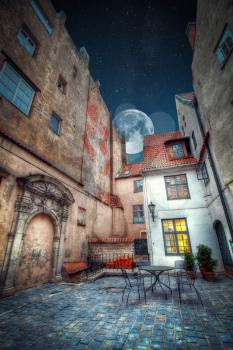 Vintage retro travel image of a narrow medieval street in old town Riga. night shining moon and stars