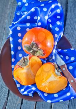 Ripe persimmons on plate and on table