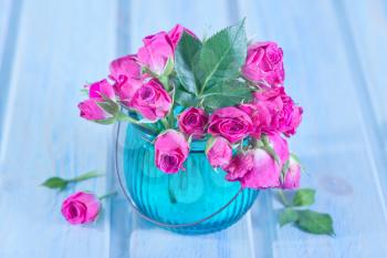Bunch of small pink Roses in a glass vase over a wooden table.