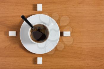 White coffee cup with saucer and sugar like a clock on a wooden brown table, top view 