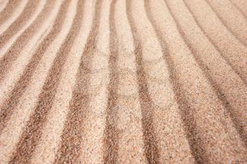 Yellow dry sand surface with grooves and wavy lines close-up perspective view with shallow depth of field nature background