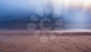 Sand on the lake beach with smooth tranquil calm water surface under soft sunset light in twilight peaceful simple natural landscape background