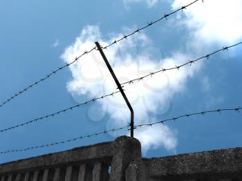 A blue sky and a dark fence with barbed wire
