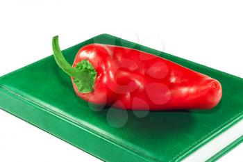 Red pepper on a green book closeup on white background