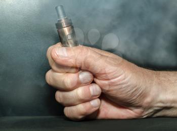 Hand with an electronic cigarette in the clouds of steam on a dark background