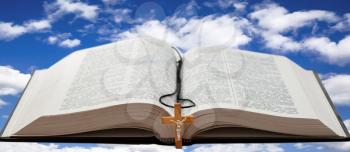 Open book with a wooden cross against a blue sky with white clouds