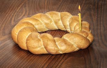 Wicker bread and a burning candle on a wooden background