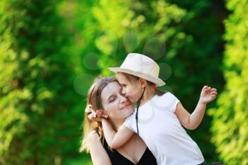 Daughter hugging her mother on the background of bright juicy green foliage. Happy family. Mom and child girl. Space for text. Shallow depth of field. Selective focus.